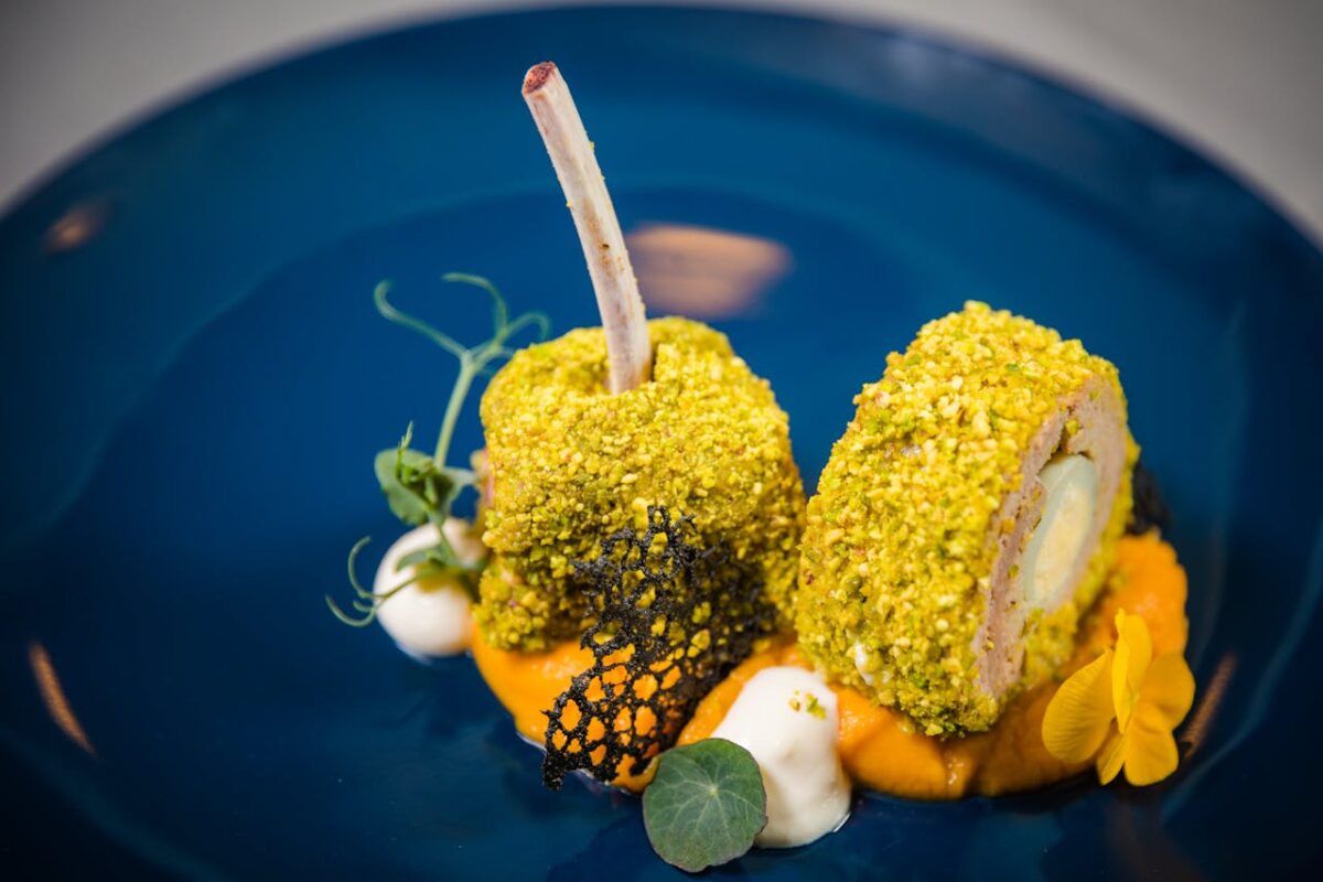 Exquisite lamb rack with pistachio crust, plated on a vibrant blue dish, showcasing fine dining artistry.