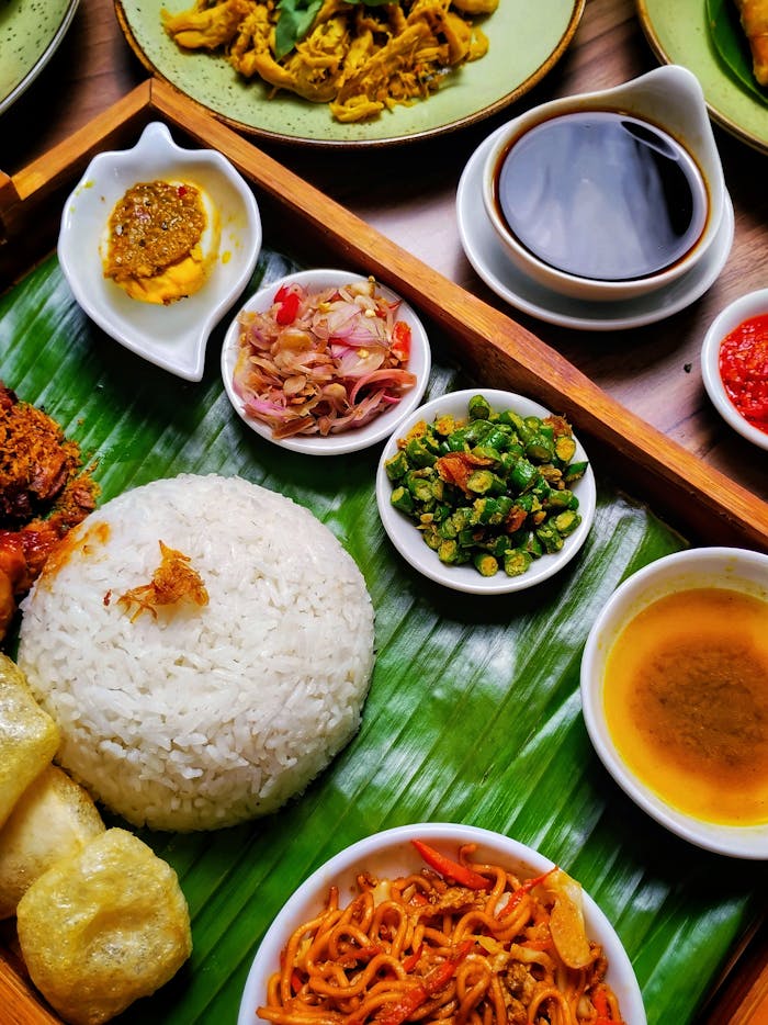 Colorful overhead shot of traditional Indonesian Nasi Padang with rice, sambal, and side dishes on banana leaves.