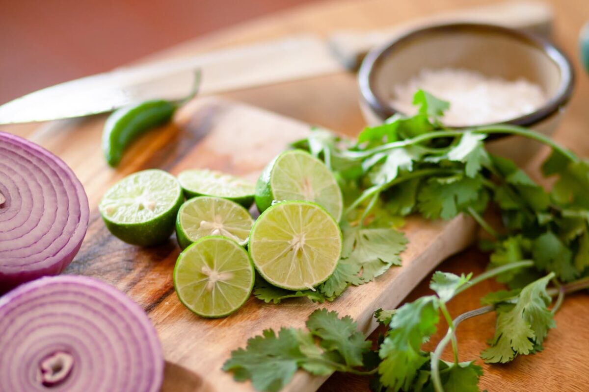 Citrus, coriander, and red onion on a cutting board for food prep.