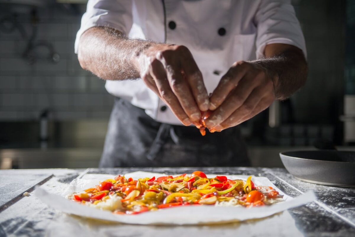 Chef adds final toppings to a colorful dish in a professional kitchen.